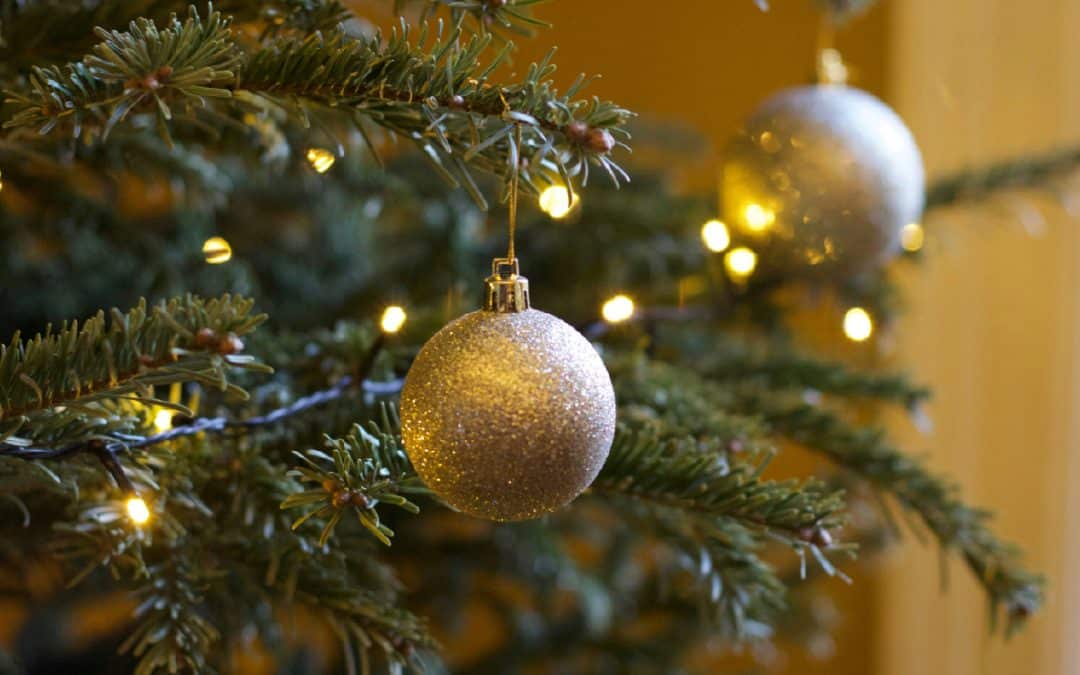 Close-up of a decorated Christmas tree branch with golden baubles and warm white string lights.